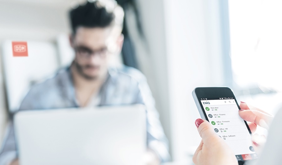 focused picture of a hand holding a phone with man with laptop as background