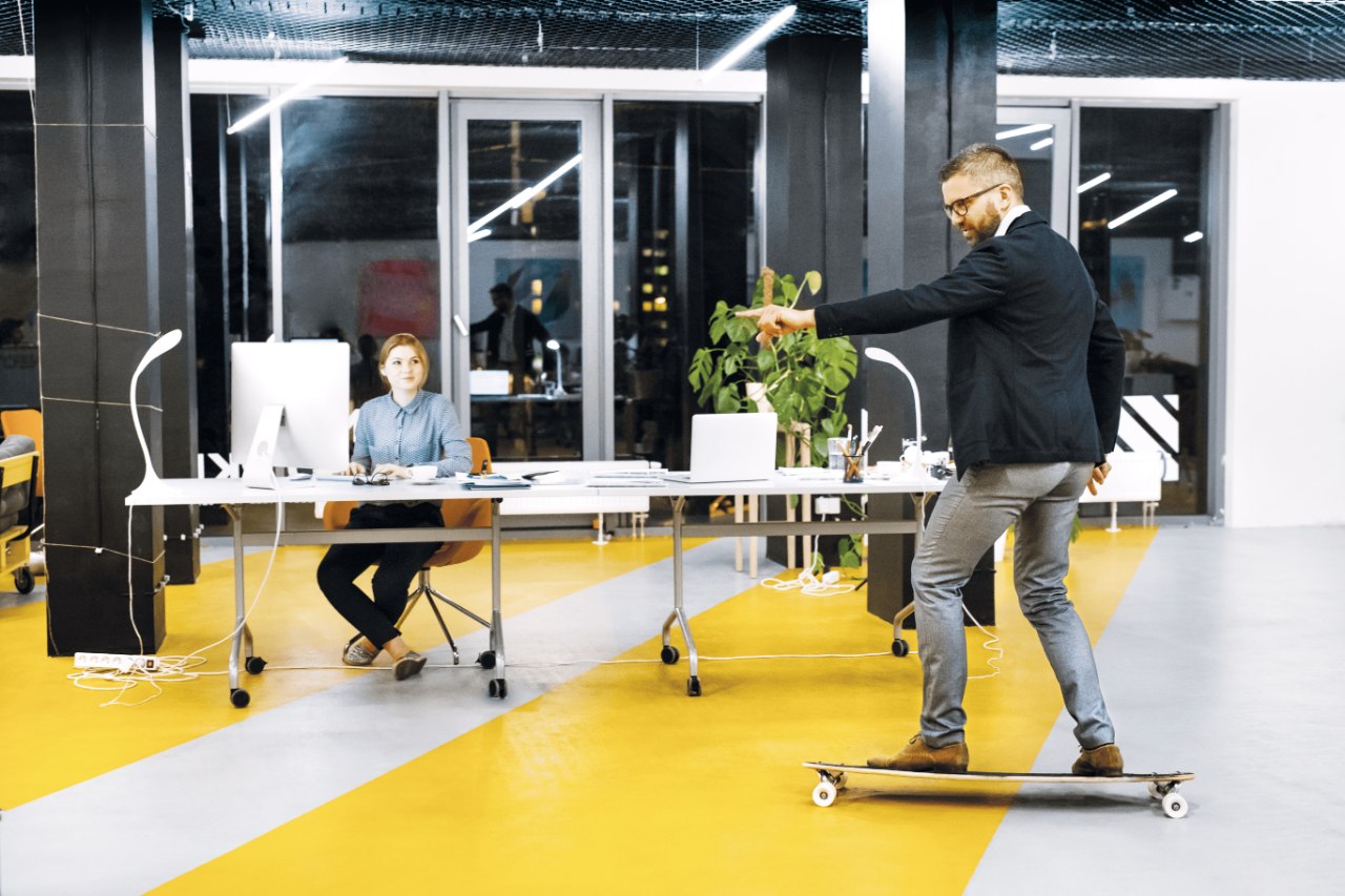 man skateboarding in an office while a woman looking at him