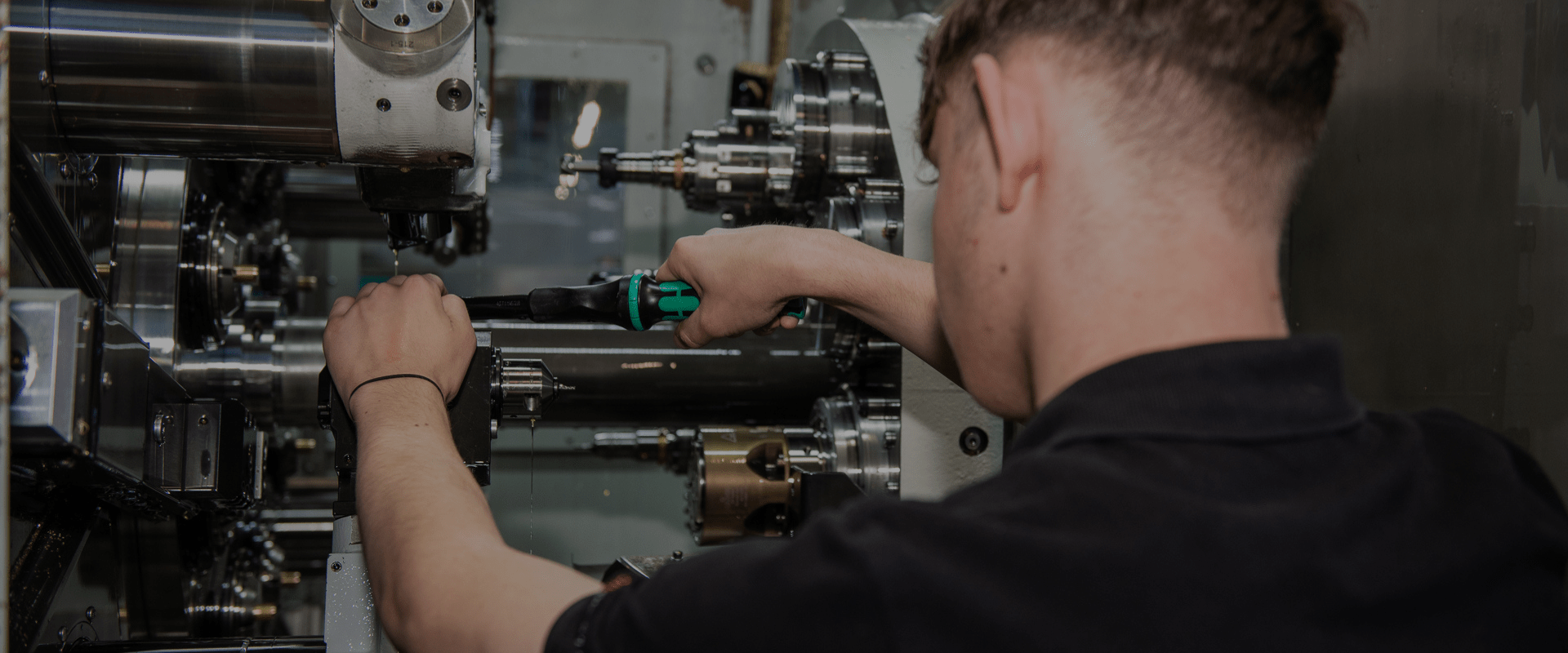 Auszubildender zum Zerspanungsmechaniker bei DOM Sicherheitstechnik richtet eine CNC-Maschine ein und führt präzise Bearbeitungsschritte an Metallbauteilen durch.