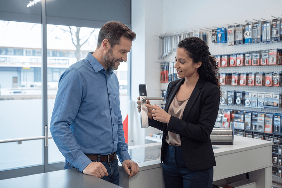 Außendienstmitarbeiterin von DOM Sicherheitstechnik berät einen Kunden zu elektronischen Zutrittssystemen und präsentiert einen digitalen Türbeschlag im Showroom.