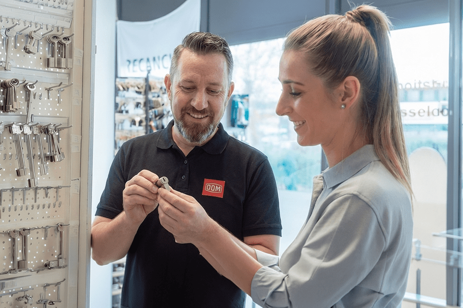 Außendienstmitarbeiter von DOM Sicherheitstechnik berät eine Kundin zu mechanischen Schließsystemen und präsentiert einen Schließzylinder im Showroom.