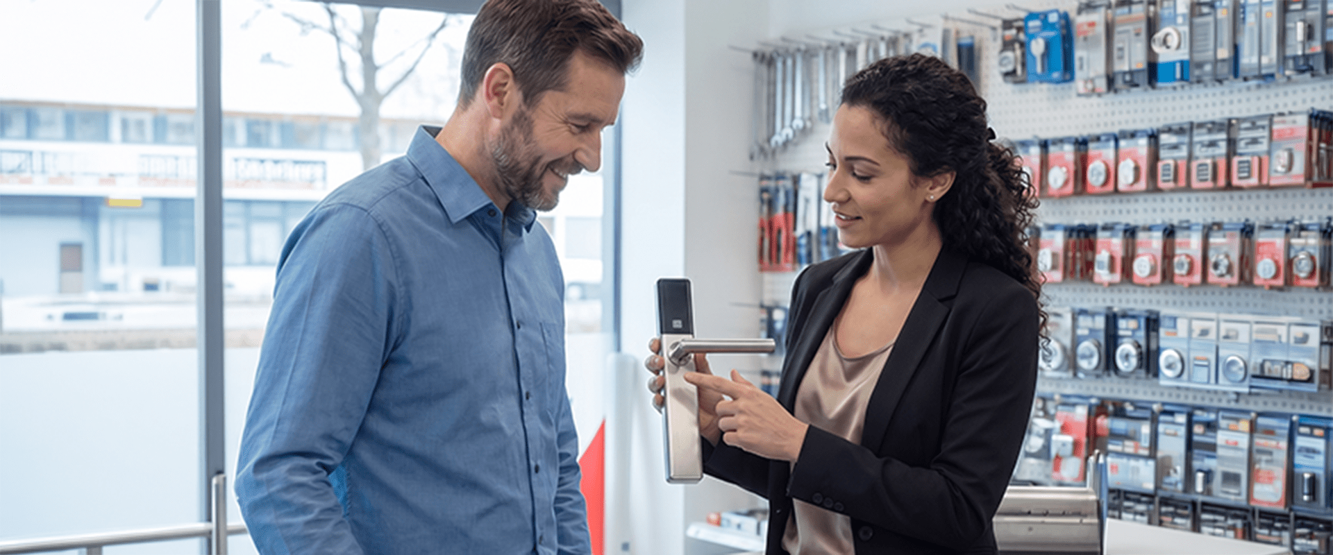 Außendienstmitarbeiterin von DOM Sicherheitstechnik berät einen Kunden zu elektronischen Zutrittssystemen und präsentiert einen digitalen Türbeschlag im Showroom.
