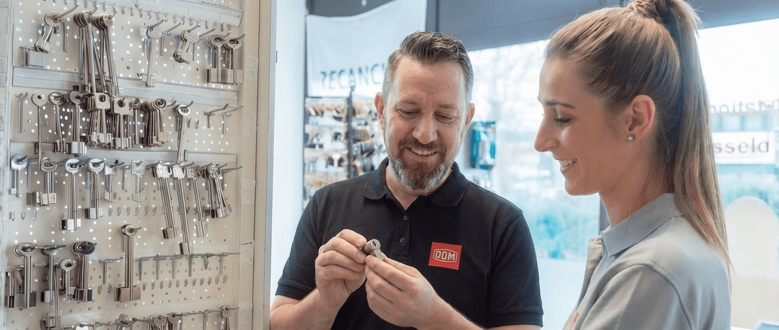 Außendienstmitarbeiter von DOM Sicherheitstechnik berät eine Kundin zu mechanischen Schließsystemen und präsentiert einen Schließzylinder im Showroom.