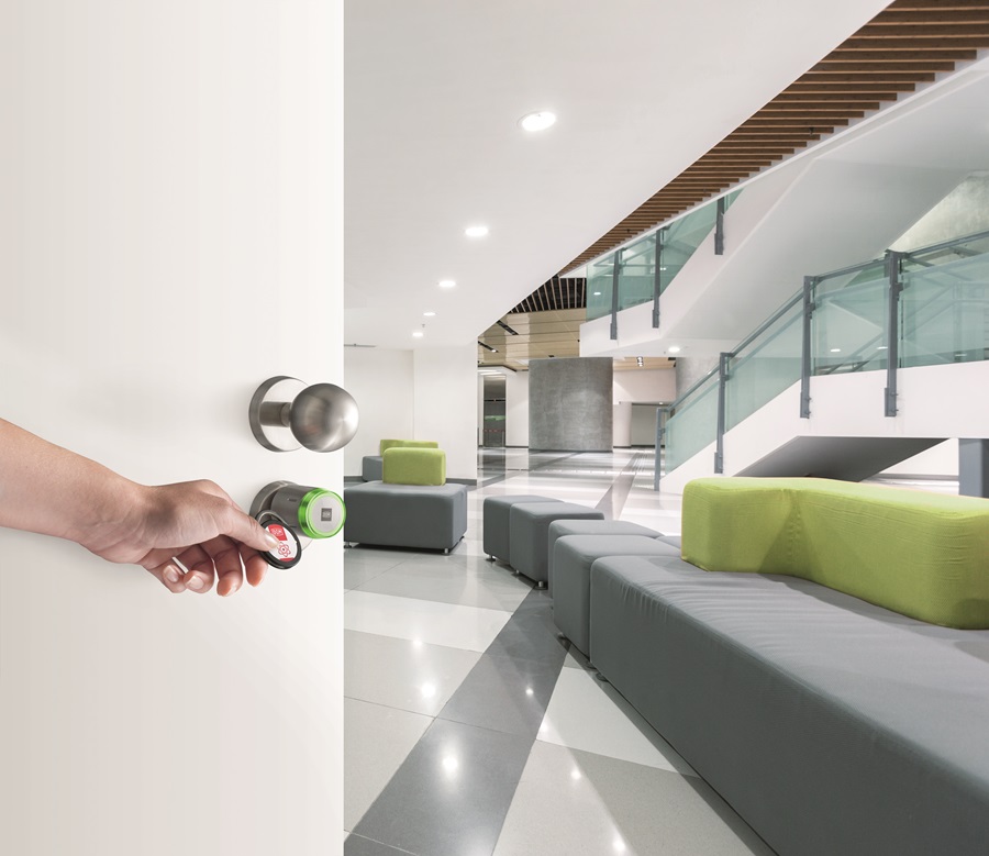 DOM ENiQ Pro Zylinder an einer Tür wird mit einem Transponder geöffnet, im Hintergund ist die Lobby eines Bürogebäudes zu sehen.