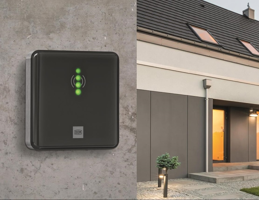 Im Vordergrund ein DOM Wandleser an einer Hausfassade montiert, im Hintergrund der Eingangsbereich des Hauses