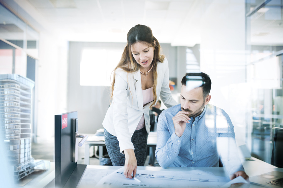 Zwei Architekt:innen unterhalten sich in einem Büro über einen Gebäudeplan