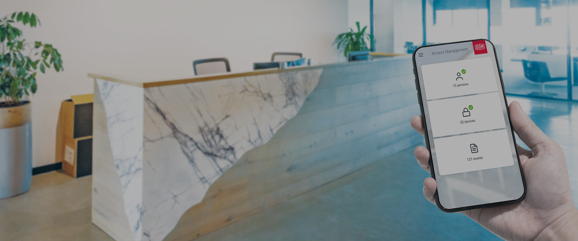 Hand, die ein Smartphone mit ENiQ App Hauptbildschirmoberfläche vor einem Empfangsbereich hält