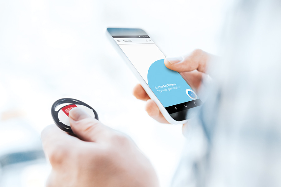 two hands, left hand holding a transponder, right hand holding a smartphone with ENiQ App interface