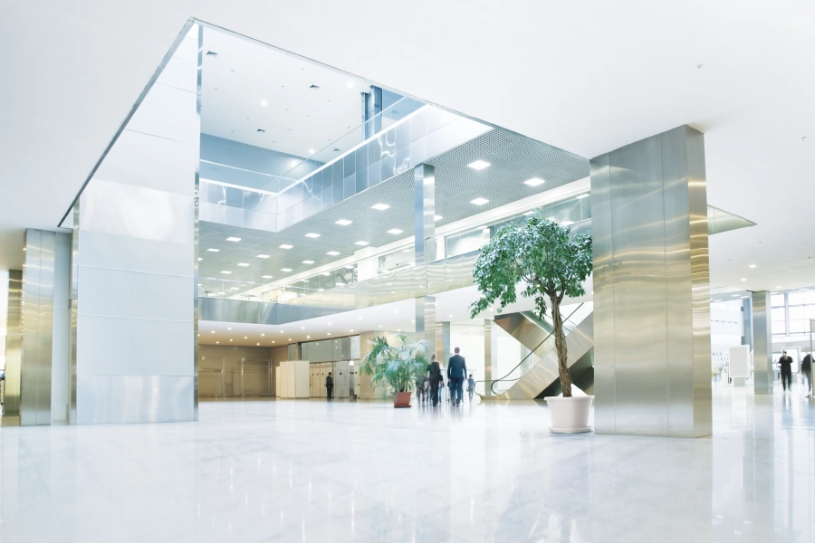 Hall luminosa di un edificio moderno con ascensore, colonne in acciaio e piante decorative.