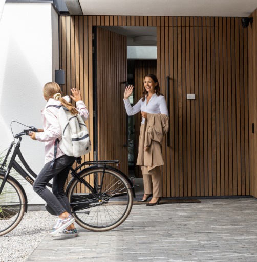 mom in the front doorway waving to her daughter who is about to leave on her bicycle