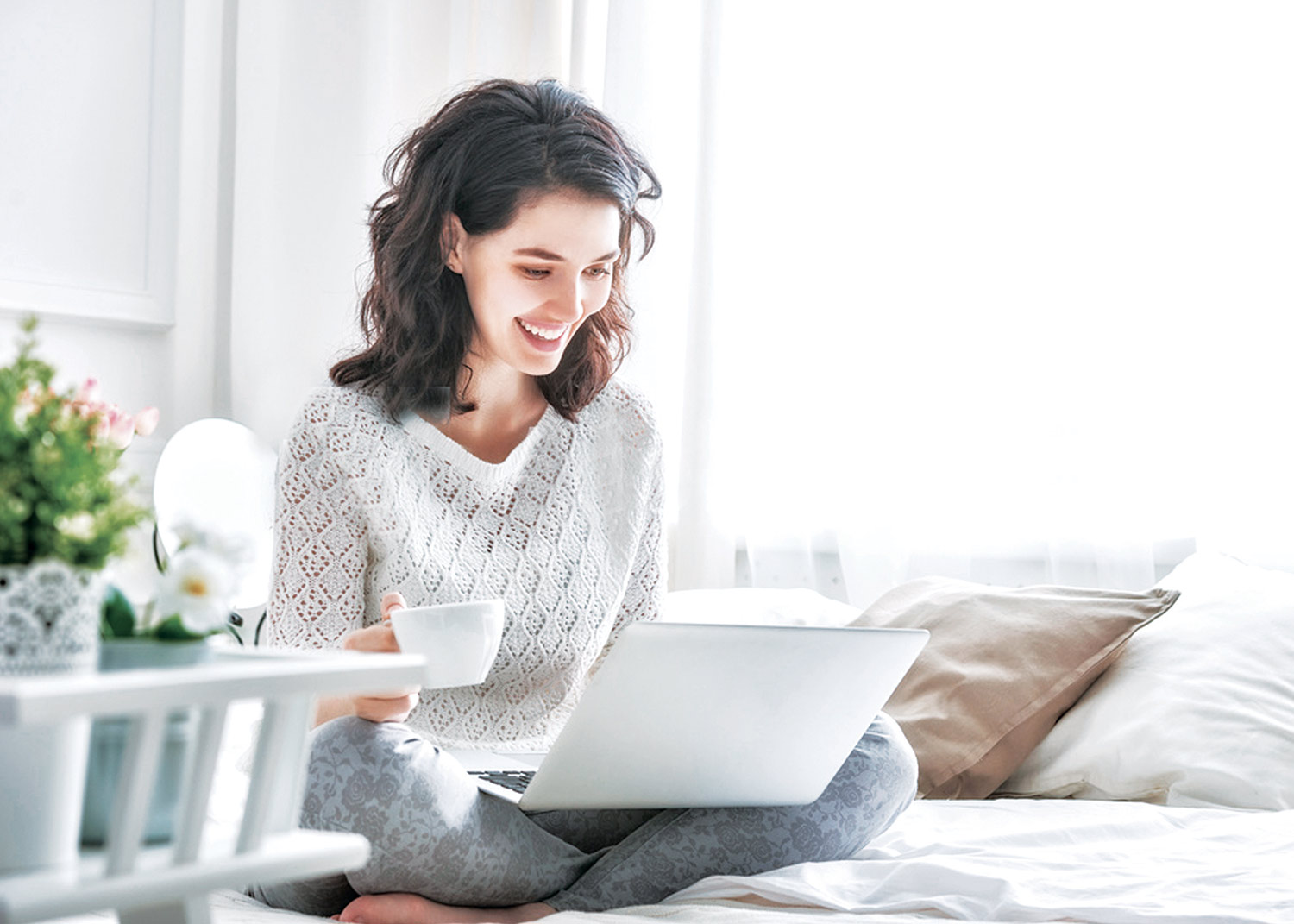 girl sitting on the bed with a cup in her hand while working on the pc