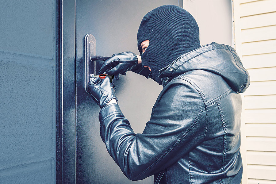 ladro con il passamontagna che tenta di aprire la porta di un'abitazione protetta da un cilindro europeo di bassa sicurezza mediante la chiave universale topolino decoder