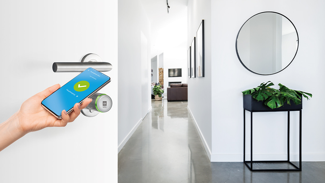 DOM Tapkey Pro at a front door is used with a smartphone, in the background a hallway